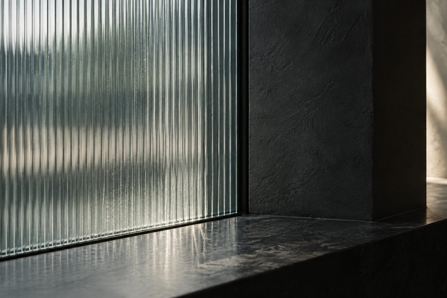 Ribbed glass beside a dark textured wall in soft silver light.