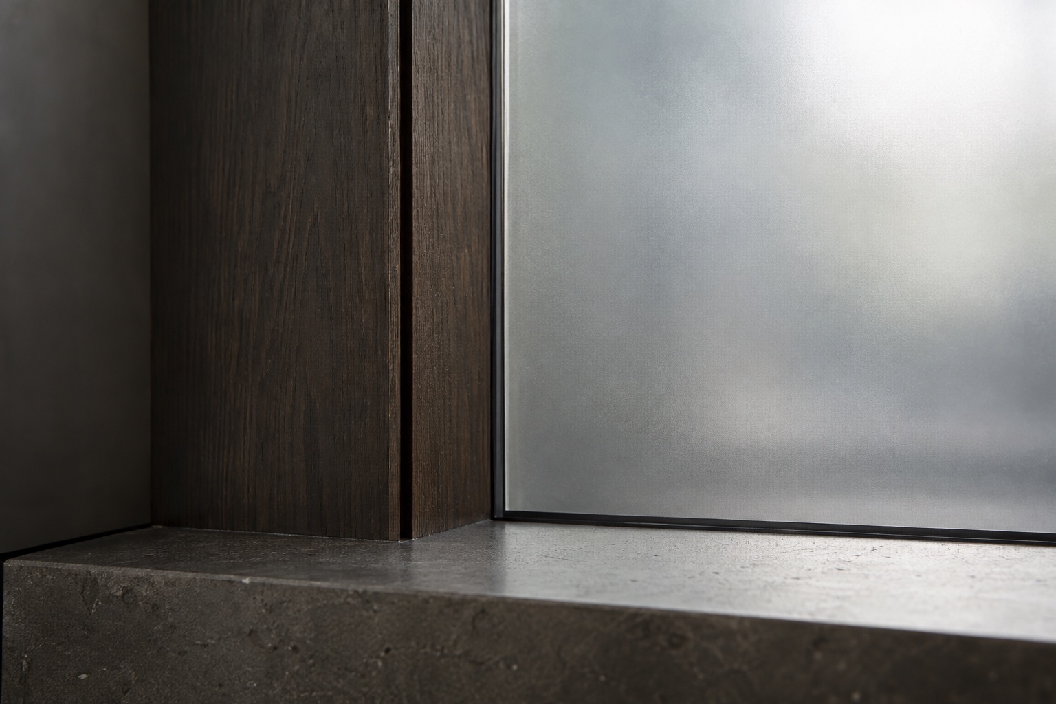 Frosted glass meeting a dark oak frame above a shallow stone ledge.