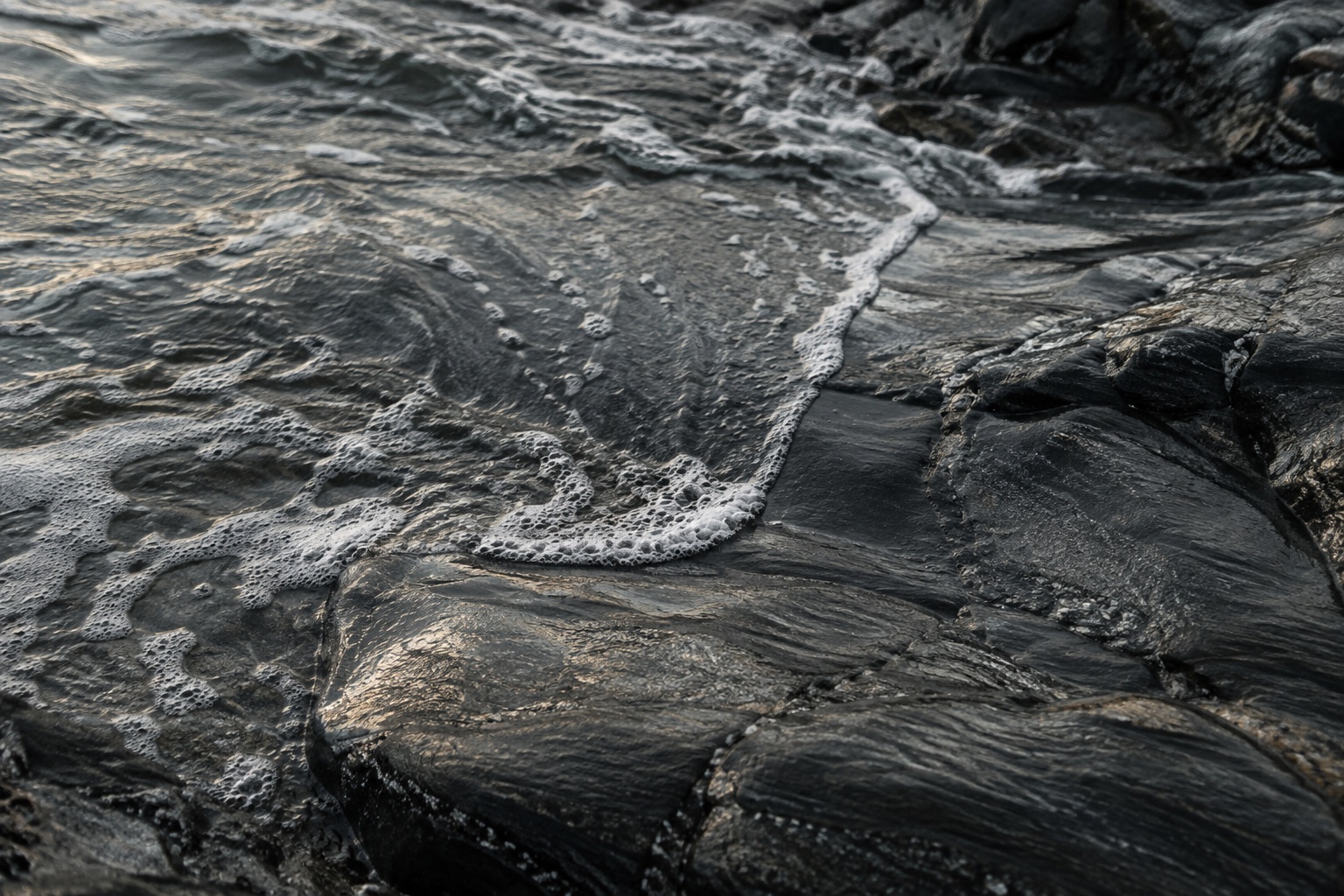 Pale water moving across dark shoreline stone.